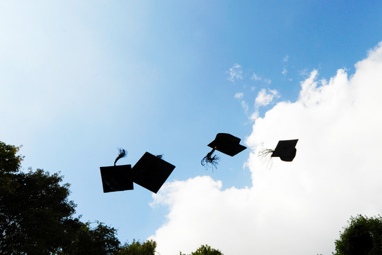 Four black doctor hats flying in the air in front of blue sky with white clouds.