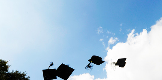 Four black doctor hats flying in the air in front of blue sky with white clouds.