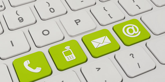 A white keyboard with four green keys. On the green keys are symbols like a telephone, a cell phone, an envelope and an „@“