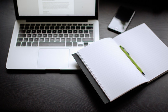 Laptop, Smartphone und Notizbuch mit Stift auf einem Tisch liegend.