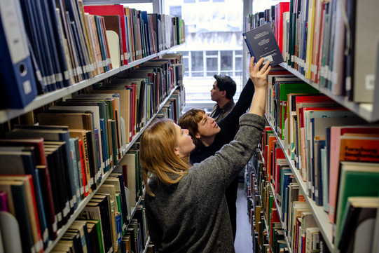 Students search for books on bookshelves in the library.