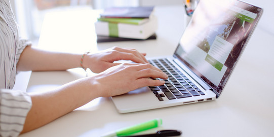 digitale Lehrevaluation Studentin tippend am Laptop, daneben liegen Bücher und Stifte.