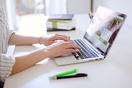 Studentin tippend am Laptop, daneben liegen Bücher und Stifte.