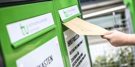 Eine Hand wirft einen Umschlag in den Fristenbriefkasten