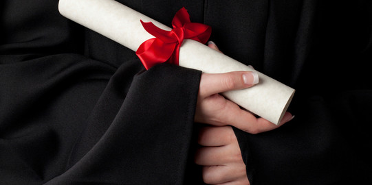 A rolled document with red bow is held by hands. 