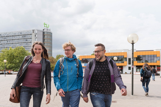 Three students walk across the cafeteria bridge and talk.