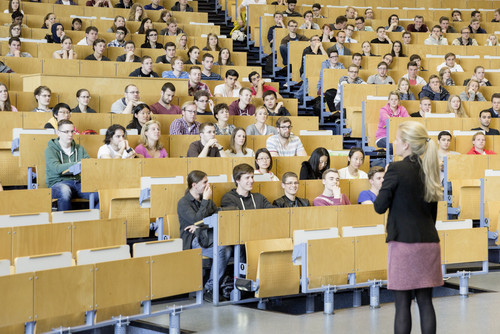 A lecturer stands in front of students in the lecture hall. 