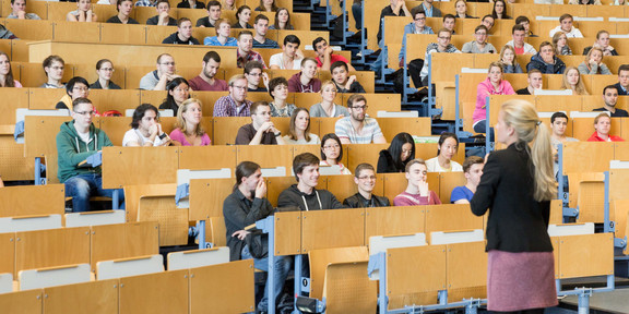 A lecturer stands in front of students in the lecture hall. 