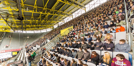 First semester students sit in the stands at the stadium during the welcoming of first-semester students and watch a show act sideways. 